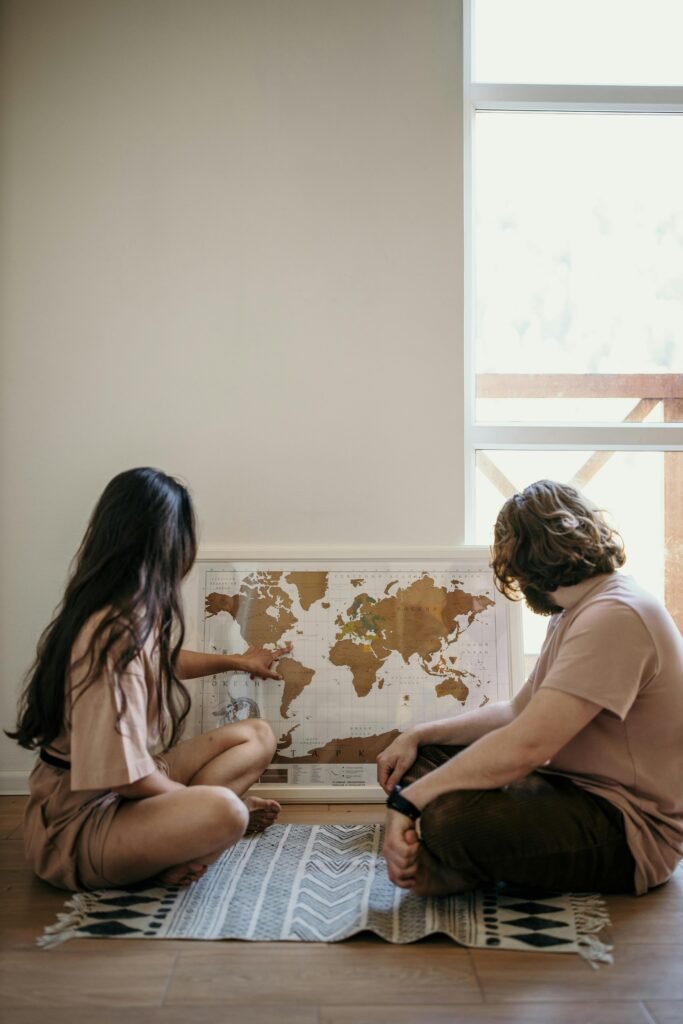 A couple sitting on the floor looks at a world map, planning their next trip indoors.