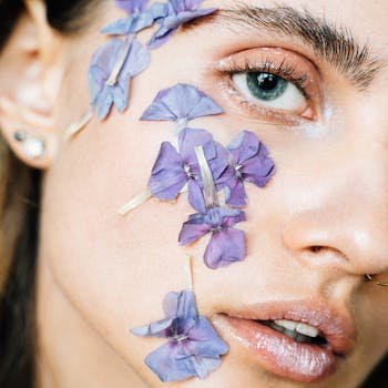 Artistic close-up portrait of a woman with purple petals on her face.