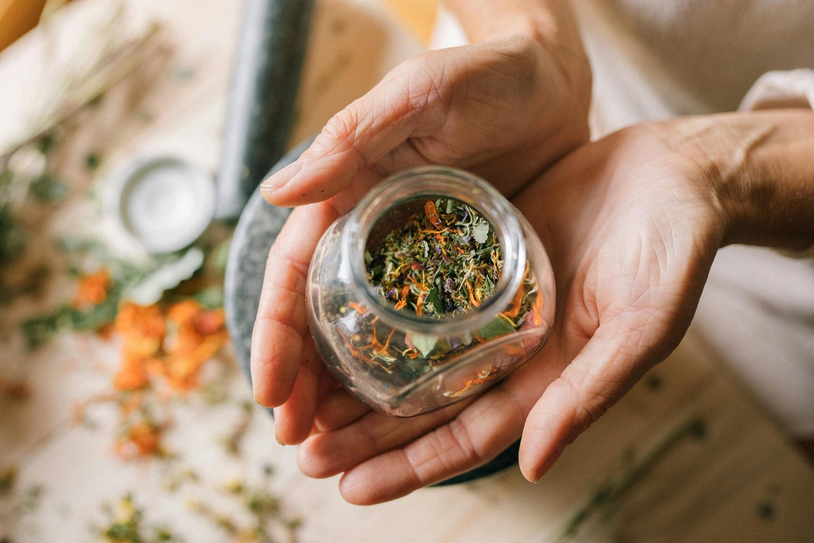 Close-up of hands holding a glass jar filled with colorful dried herbs.