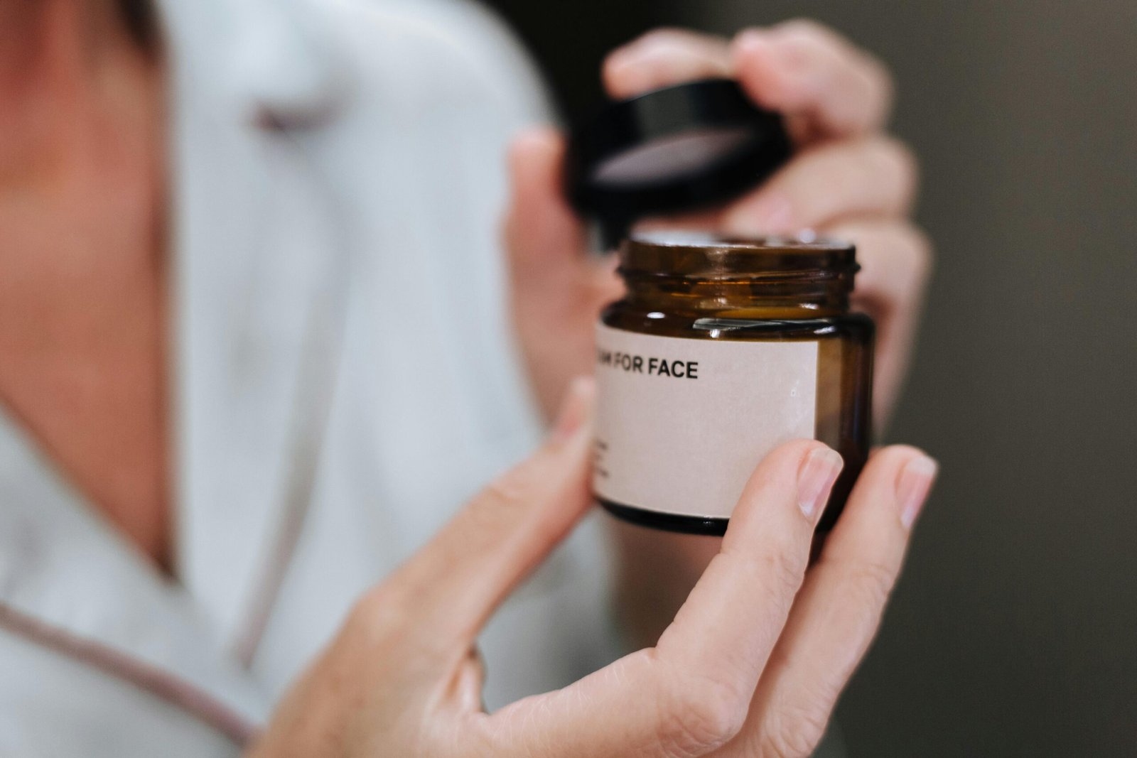 Detailed shot of hands opening a face cream jar, highlighting skincare routine.