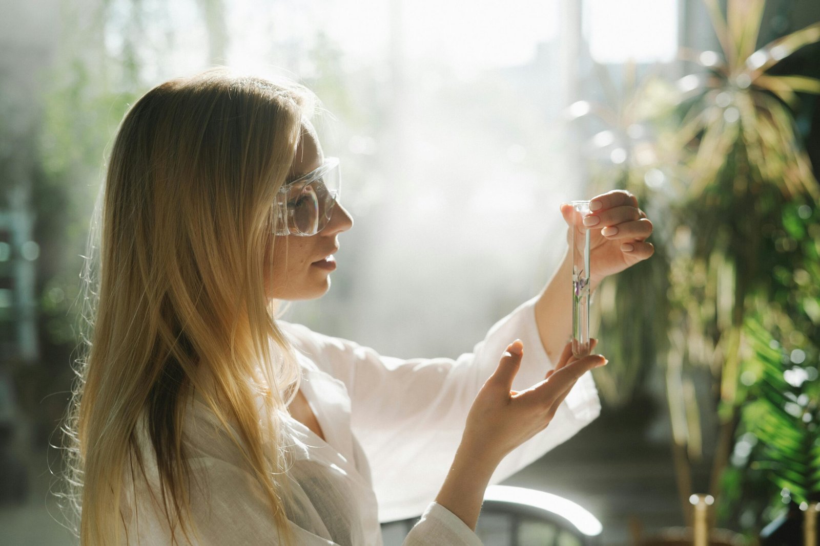 Side view of a woman with blond hair examining a test tube in a sunny lab.