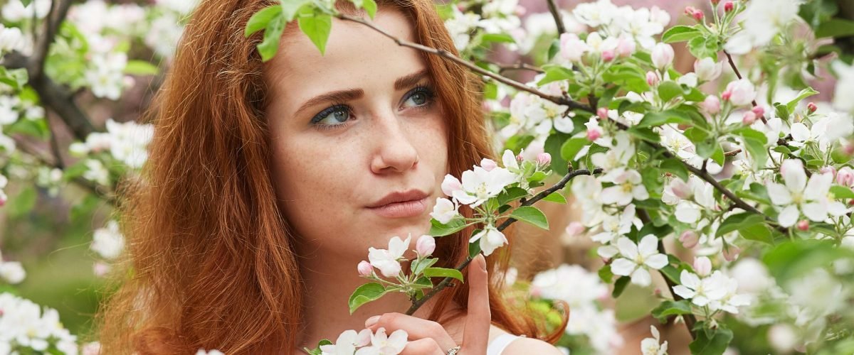 A redhead woman surrounded by blooming apple blossoms in a lush Moscow orchard. Captivating springtime serenity.